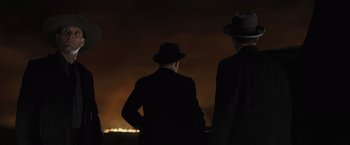 Movie still from “Killers of the Flower Moon” (2023), directed by Martin Scorsese – A couple of men standing next to each other in front of a fire; Medium shot, High angle