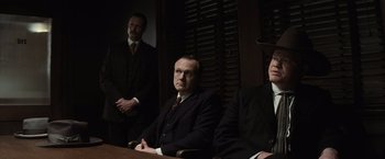 Movie still from “Killers of the Flower Moon” (2023), directed by Martin Scorsese – A group of men sitting at a table in a dark room; Medium shot, Low angle