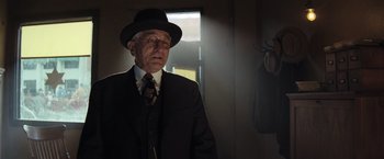 Movie still from “Killers of the Flower Moon” (2023), directed by Martin Scorsese – An older man in a suit and hat in a dark room; Medium shot, Over the shoulder angle