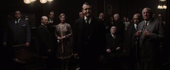 Movie still from “Killers of the Flower Moon” (2023), directed by Martin Scorsese – A group of men and women standing in a room; Medium shot, Over the shoulder angle