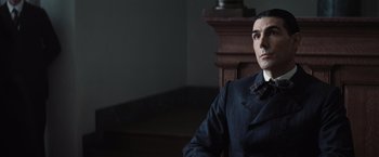 Movie still from “Killers of the Flower Moon” (2023), directed by Martin Scorsese – A man sitting in a chair wearing a suit and tie; Close Up shot, Low angle