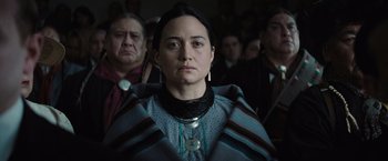 Movie still from “Killers of the Flower Moon” (2023), directed by Martin Scorsese – A woman in a native american dress looking at the camera; Close Up shot, Over the shoulder angle