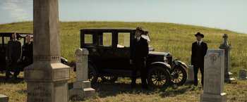 Movie still from “Killers of the Flower Moon” (2023), directed by Martin Scorsese – A man standing next to an old car in a grassy field; Wide shot, Low angle
