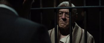 Movie still from “Killers of the Flower Moon” (2023), directed by Martin Scorsese – An old man with glasses is behind bars in a jail cell; Close Up shot, Low angle