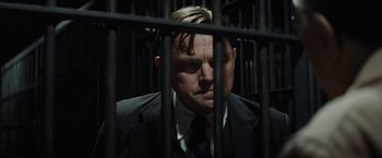 Movie still from “Killers of the Flower Moon” (2023), directed by Martin Scorsese – A man wearing a suit and tie behind bars; Close Up shot, Low angle
