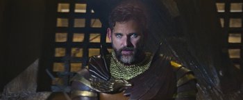 Movie still from “King Arthur: Legend of the Sword” (2017), directed by Guy Ritchie – A man with a beard wearing a costume and holding an eagle; Close Up shot, Over the shoulder angle