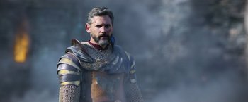 Movie still from “King Arthur: Legend of the Sword” (2017), directed by Guy Ritchie – A man with a beard wearing a suit of armor; Medium shot, Over the shoulder angle