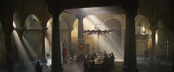 Movie still from “King Arthur: Legend of the Sword” (2017), directed by Guy Ritchie – A group of people sitting around a table in a room; Extreme Wide shot, Low angle