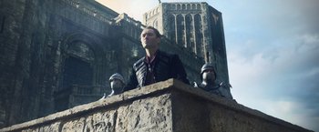 Movie still from “King Arthur: Legend of the Sword” (2017), directed by Guy Ritchie – A man standing on top of a building next to two other men; Medium shot, Low angle