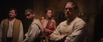 Movie still from “King Arthur: Legend of the Sword” (2017), directed by Guy Ritchie – A group of people sitting in a room with candles; Medium shot, Over the shoulder angle