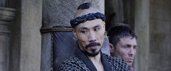 Movie still from “King Arthur: Legend of the Sword” (2017), directed by Guy Ritchie – A man with a beard and a turban on his head; Close Up shot, Over the shoulder angle