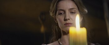 Movie still from “King Arthur: Legend of the Sword” (2017), directed by Guy Ritchie – A beautiful woman looking at a lit candle in the dark; Close Up shot, Over the shoulder angle
