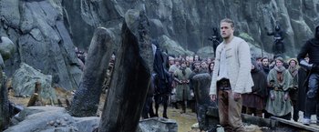 Movie still from “King Arthur: Legend of the Sword” (2017), directed by Guy Ritchie – A group of people standing around a stone wall; Wide shot, Low angle