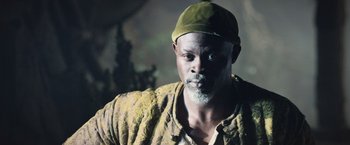 Movie still from “King Arthur: Legend of the Sword” (2017), directed by Guy Ritchie – A man with a beard wearing a hat and jacket; Close Up shot, Low angle