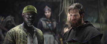 Movie still from “King Arthur: Legend of the Sword” (2017), directed by Guy Ritchie – A man with a beard standing next to another man with a beard; Medium shot, Over the shoulder angle