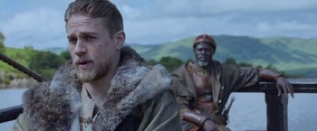 Movie still from “King Arthur: Legend of the Sword” (2017), directed by Guy Ritchie – Two men sitting on a bench in a field; Close Up shot, Over the shoulder angle