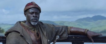 Movie still from “King Arthur: Legend of the Sword” (2017), directed by Guy Ritchie – An old man with a beard and a red hat is posing for a picture; Close Up shot, Low angle