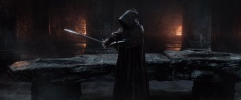 Movie still from “King Arthur: Legend of the Sword” (2017), directed by Guy Ritchie – A person in a hooded cloak holding a sword; Wide shot, Over the shoulder angle