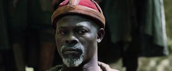 Movie still from “King Arthur: Legend of the Sword” (2017), directed by Guy Ritchie – An older man wearing a red and white hat; Close Up shot, Low angle