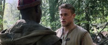 Movie still from “King Arthur: Legend of the Sword” (2017), directed by Guy Ritchie – A man with long hair talking to another man in medieval garb; Close Up shot, Over the shoulder angle