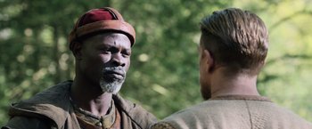 Movie still from “King Arthur: Legend of the Sword” (2017), directed by Guy Ritchie – A man with a beard and a red hat talking to another man; Close Up shot, Over the shoulder angle