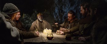 Movie still from “King Arthur: Legend of the Sword” (2017), directed by Guy Ritchie – A group of people sitting around a table with candles; Medium shot, Over the shoulder angle