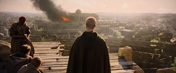 Movie still from “King Arthur: Legend of the Sword” (2017), directed by Guy Ritchie – A man wearing a cape standing in front of a burning building; Extreme Wide shot, High angle