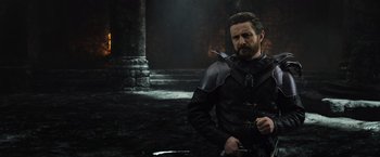 Movie still from “King Arthur: Legend of the Sword” (2017), directed by Guy Ritchie – A man with a sword in his hand standing next to a wall; Medium shot, Over the shoulder angle