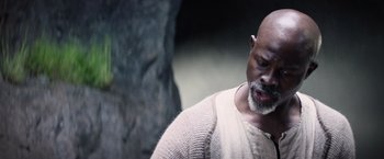 Movie still from “King Arthur: Legend of the Sword” (2017), directed by Guy Ritchie – An older bald man wearing a white sweater; Close Up shot, Low angle