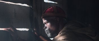 Movie still from “King Arthur: Legend of the Sword” (2017), directed by Guy Ritchie – A man wearing a red hat looking out a window; Close Up shot, Low angle