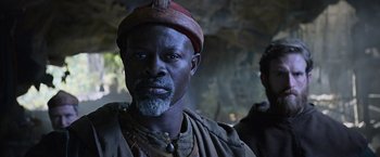 Movie still from “King Arthur: Legend of the Sword” (2017), directed by Guy Ritchie – A person with a beard wearing a hat; Close Up shot, Over the shoulder angle