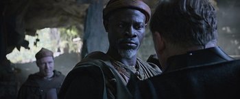 Movie still from “King Arthur: Legend of the Sword” (2017), directed by Guy Ritchie – A man with a beard and a hat is talking to another man; Close Up shot, Over the shoulder angle