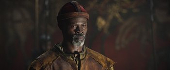 Movie still from “King Arthur: Legend of the Sword” (2017), directed by Guy Ritchie – A man with a beard wearing a hat and a leather jacket; Close Up shot, Over the shoulder angle