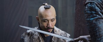 Movie still from “King Arthur: Legend of the Sword” (2017), directed by Guy Ritchie – A man with a shaved head holding a sword in his hand; Close Up shot, Over the shoulder angle