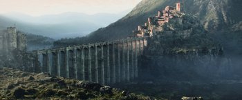 Movie still from “King Arthur: Legend of the Sword” (2017), directed by Guy Ritchie – A view of a mountain with a bridge in the middle of it; Extreme Wide shot, Low angle
