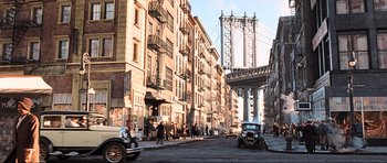 Movie still from “King Kong” (2005), directed by Peter Jackson – A street scene with a bridge in the background and people walking on the sidewalk; Extreme Wide shot, High angle
