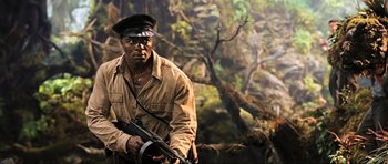 Movie still from “King Kong” (2005), directed by Peter Jackson – An african american man holding a rifle in front of a painting; Medium shot, Low angle
