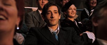 Movie still from “King Kong” (2005), directed by Peter Jackson – A man in a suit and tie sitting in front of other people; Close Up shot, Over the shoulder angle