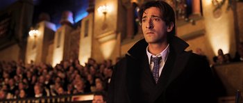 Movie still from “King Kong” (2005), directed by Peter Jackson – A man wearing a suit and tie in front of an audience; Close Up shot, Low angle