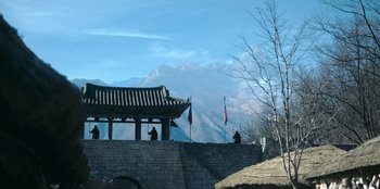 Movie still from “Kingdom: Ashin of the North” (2021), directed by Kim Seong-hun – Two people sitting on a stone wall near a building; Extreme Wide shot, Over the shoulder angle