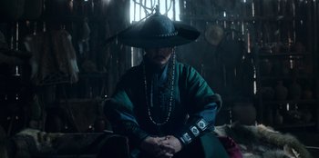 Movie still from “Kingdom: Ashin of the North” (2021), directed by Kim Seong-hun – A man wearing a hat sitting down in a room; Medium shot, Low angle