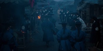 Movie still from “Kingdom: Ashin of the North” (2021), directed by Kim Seong-hun – A group of people standing around a bonfire; Wide shot, Over the shoulder angle