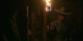 Movie still from “Kingdom: Ashin of the North” (2021), directed by Kim Seong-hun – A person in a hat is holding a candle in the dark; Medium shot, Low angle