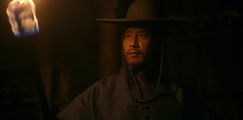 Movie still from “Kingdom: Ashin of the North” (2021), directed by Kim Seong-hun – A man wearing a hat and a long necklace; Close Up shot, Low angle