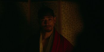 Movie still from “Kingdom: Ashin of the North” (2021), directed by Kim Seong-hun – A man wearing a robe and a baseball cap; Close Up shot, Over the shoulder angle