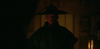 Movie still from “Kingdom: Ashin of the North” (2021), directed by Kim Seong-hun – A man with a hat is standing in the dark; Close Up shot, Over the shoulder angle