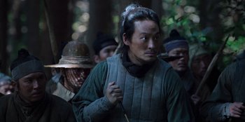 Movie still from “Kingdom: Ashin of the North” (2021), directed by Kim Seong-hun – A group of people in the woods with one man smoking a pipe; Medium shot, Low angle