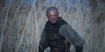 Movie still from “Kingdom: Ashin of the North” (2021), directed by Kim Seong-hun – A man with a beard in a field of tall grass; Medium shot, Low angle