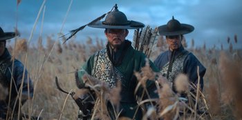 Movie still from “Kingdom: Ashin of the North” (2021), directed by Kim Seong-hun – Two men are standing in a field holding arrows; Medium shot, Low angle