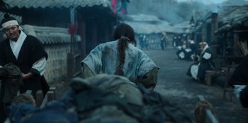 Movie still from “Kingdom: Ashin of the North” (2021), directed by Kim Seong-hun – A woman with a long braid walking down a street; Medium shot, Over the shoulder angle